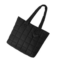 Load image into Gallery viewer, Black quilted tote bag with heart charm laid flat at an angle.