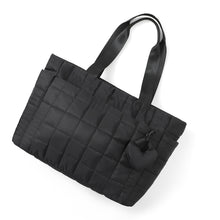 Load image into Gallery viewer, Flat lay of Nollia Emilia black quilted tote bag with heart keychain charm and double straps